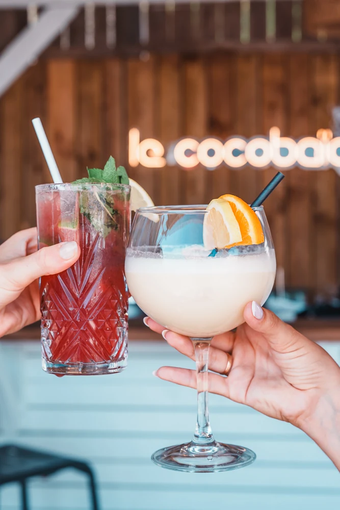 Deux cocktails levés devant l’enseigne du Cocobaïa